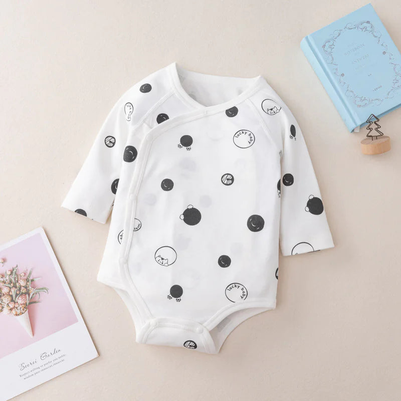 A beige long-sleeve newborn romper with open buttons at the bottom, displayed on a neutral background with decorative items around it.