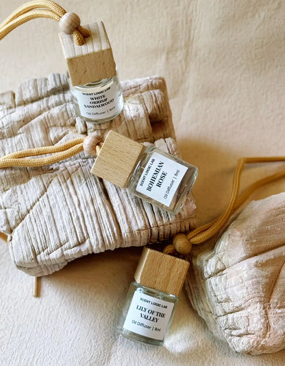 A set of holiday scented diffusers designed for use in cars, with glass bottles, wooden blocks, and labels, displayed on a neutral background.