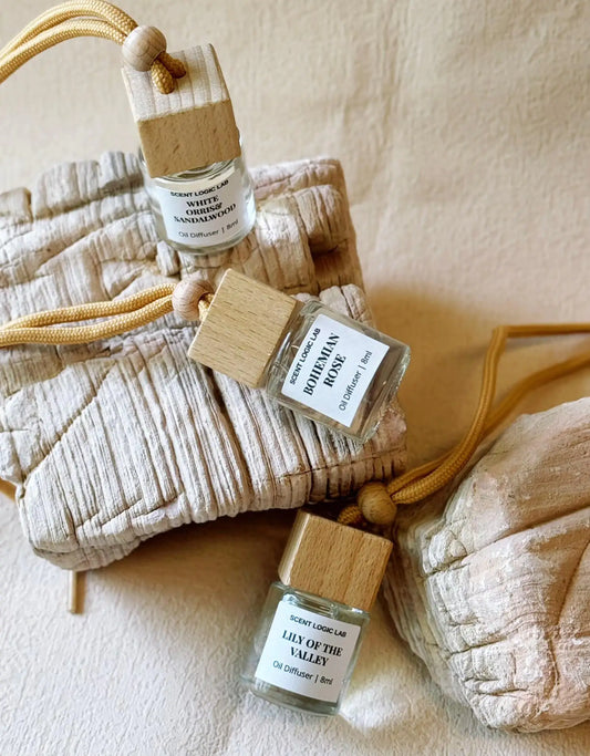 A set of holiday scented diffusers designed for use in cars, with glass bottles, wooden blocks, and labels, displayed on a neutral background.