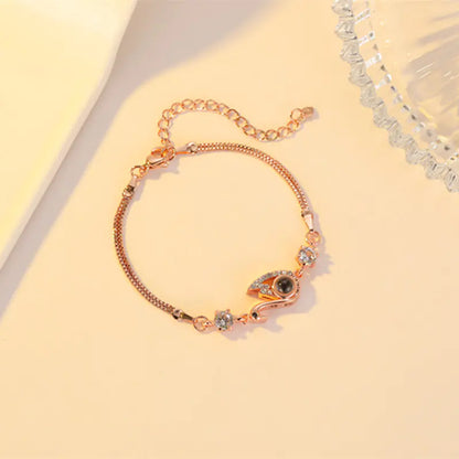 A rose gold-colored bracelet featuring a black swan charm with zirconia accents on a chain-link design, displayed against a beige background.