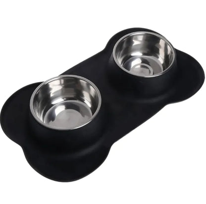 A black silicone pet bowl mat in a bone shape, with two stainless steel bowls placed on it.