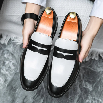 A pair of black and white leather slip-on shoes being held by a person, featuring a round toe style and low top design.