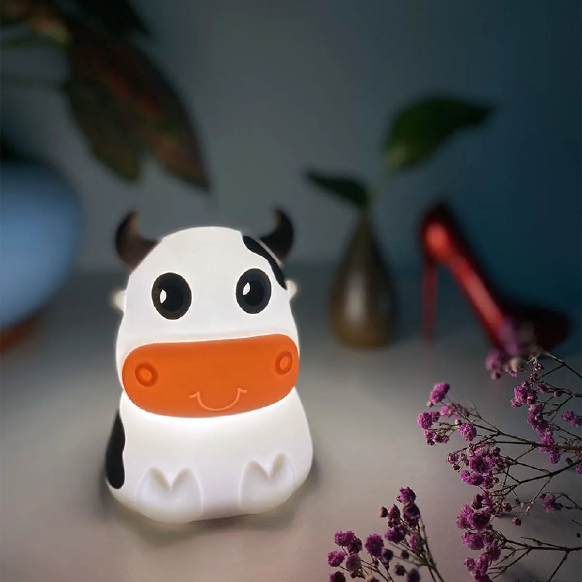 A cartoon-inspired cow-shaped silicone Bluetooth speaker and lamp with LED lighting, displayed in a room setting.