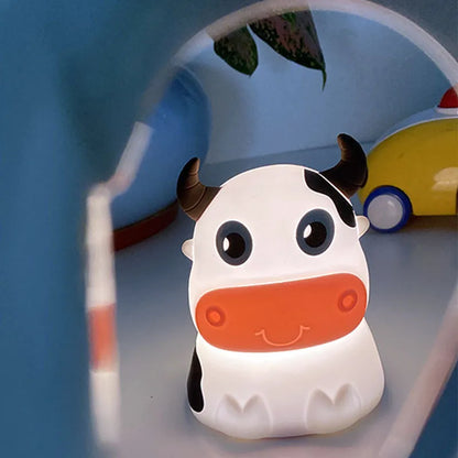 A cartoon-inspired cow-shaped silicone Bluetooth speaker and lamp with LED lighting, displayed in a room setting.