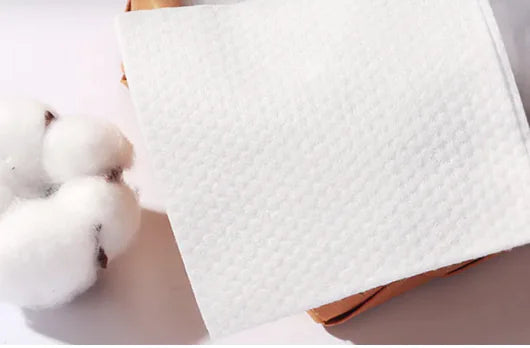 Close-up of textured white fabric with cotton balls in the background