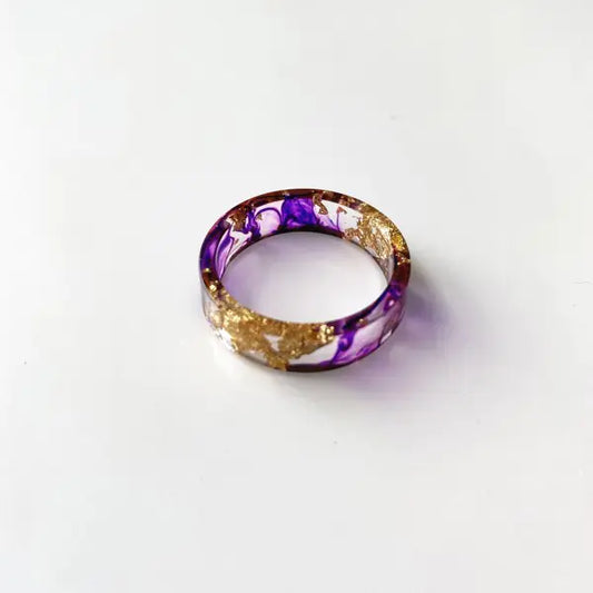 A colorful handmade resin ring with dried flowers and gold foil, displayed on a white background.