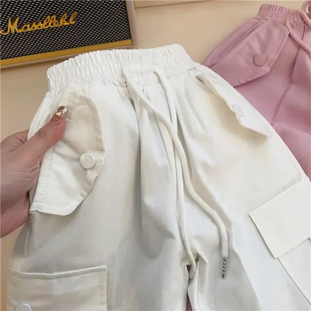 A pair of white cargo pants for infants, showcasing the texture and detail of the fabric. The pants have a mid-waist design and feature pockets and a drawstring waistband.