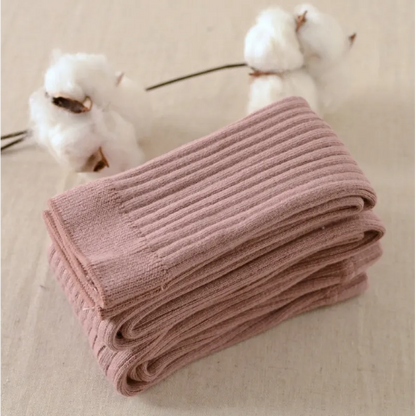 A pair of brown cotton leggings folded and placed on a flat surface with cotton flowers in the background.