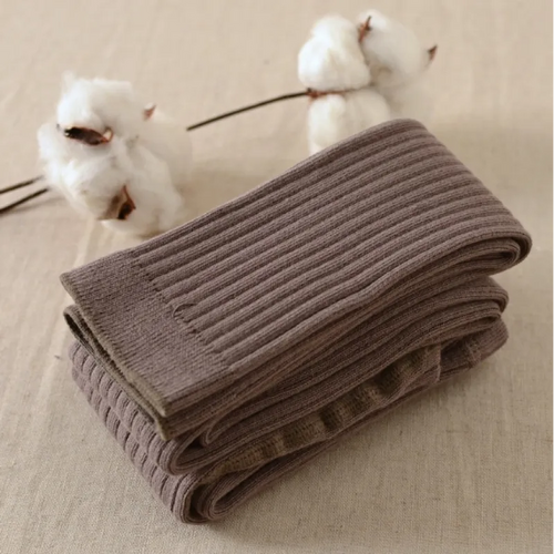 A pair of brown cotton leggings folded and placed on a flat surface with cotton flowers in the background.