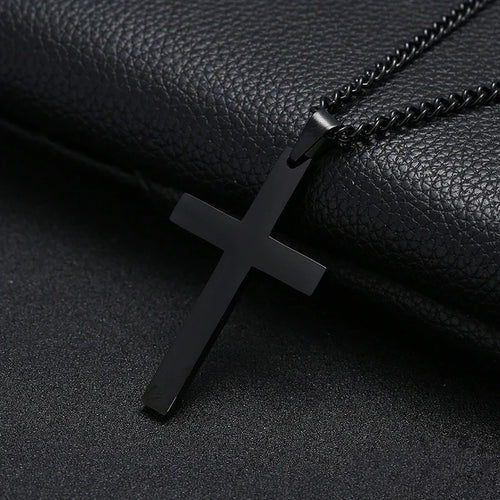 A black cross necklace made of stainless steel, displayed against a black leather background.
