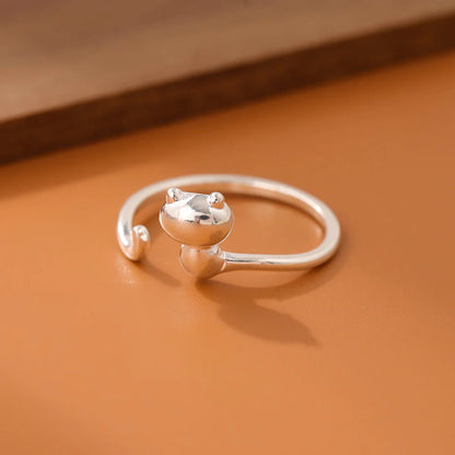 A silver-colored metal ring with a simple cat design on a brown surface.