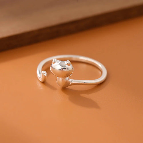 A silver-colored metal ring with a simple cat design on a brown surface.