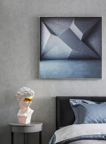A sculpture of a classical art figure placed on a side table next to a bed, with a framed abstract painting hanging on the wall above.