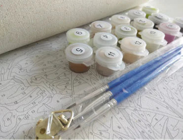 A collection of small paint jars with brushes, sponges, and a pre-printed canvas, indicating a DIY oil painting kit.