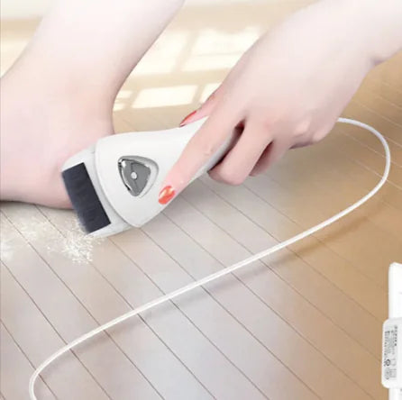 A person is using an electric pedicure device to remove calluses from their foot, which is placed on a wooden floor.