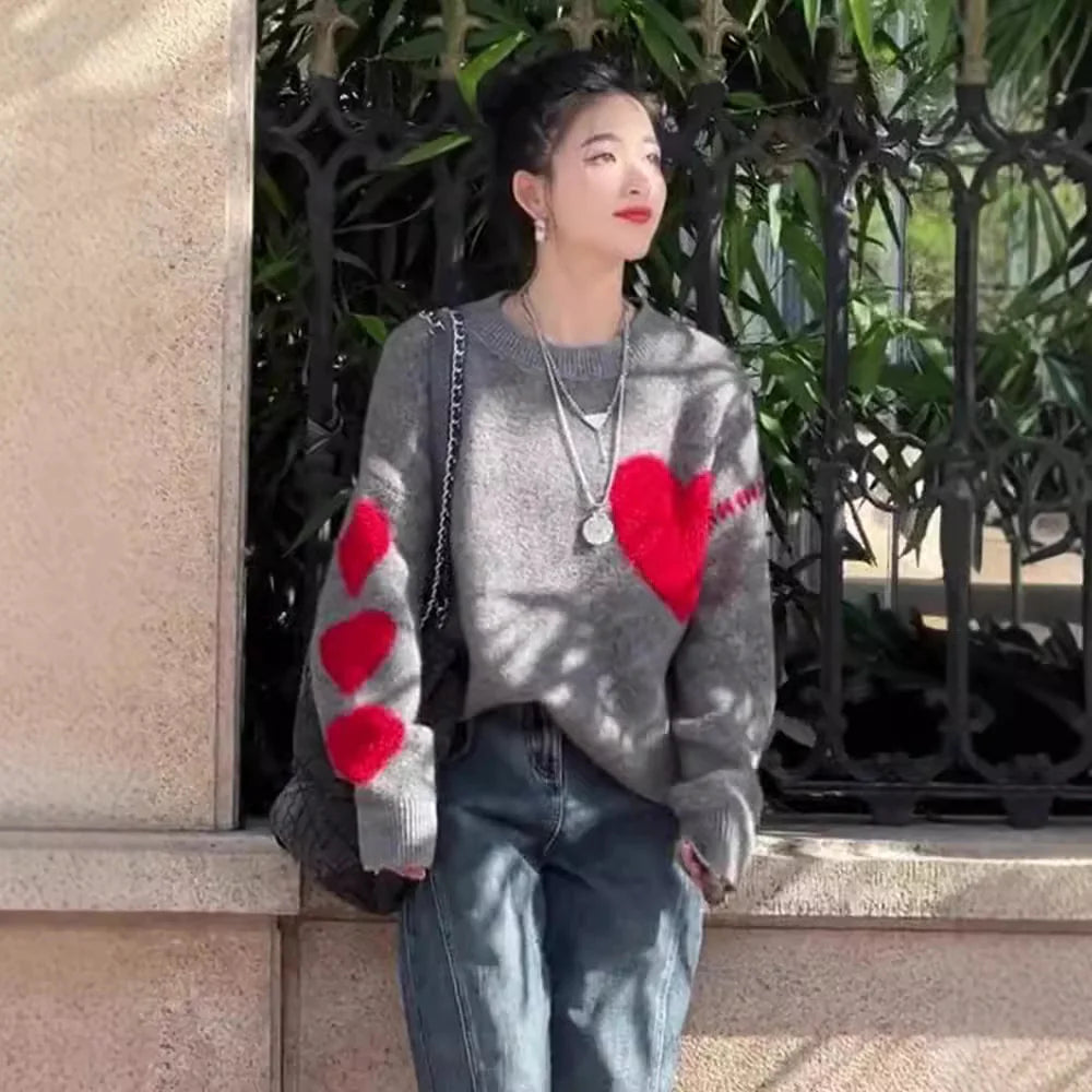 A woman wearing a gray knitted sweater with red heart patterns on the sleeves, paired with blue jeans.