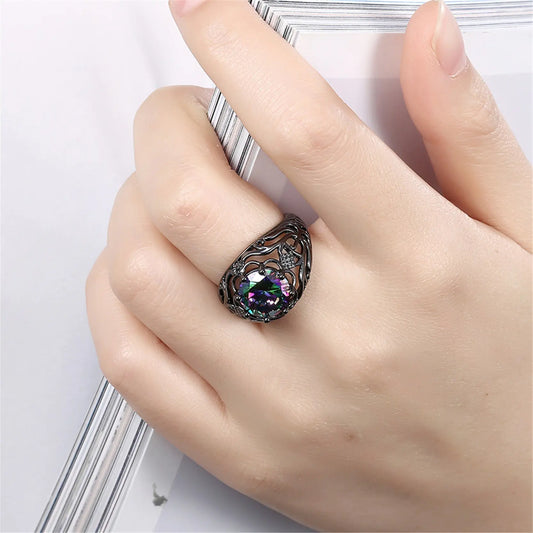 A woman's hand displaying a black gold ring with a hollow design and a purple artificial gemstone in the center.