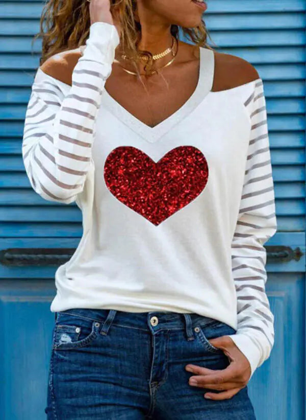 A woman wearing a white V-neck off-shoulder printed t-shirt with red heart design, paired with blue jeans.