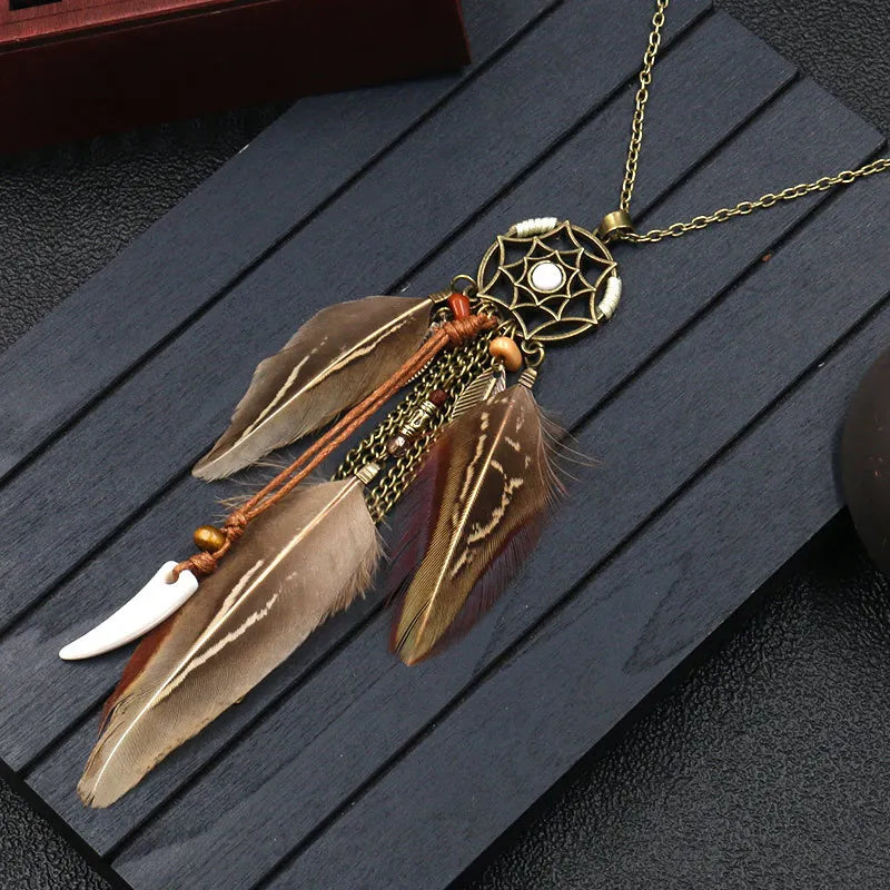 A bohemian feather dream catcher necklace with a round dream catcher design, featuring flowing feathers in brown and white tones, and a white bead at the center.