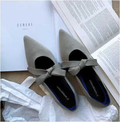 A pair of yellow flat casual boat shoes with bow Mary Jane style on a carpeted floor, surrounded by a white ribbon, a rose, and a pair of scissors.