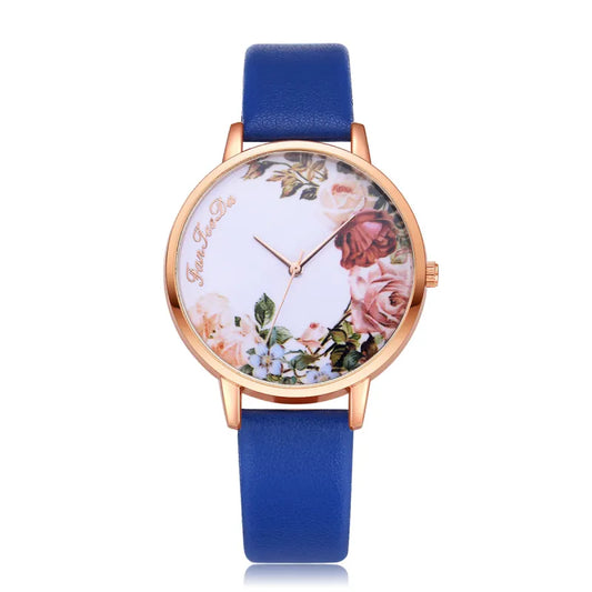 A floral pattern watch with a blue strap and gold-colored case, featuring a white dial adorned with a multicolored floral design.