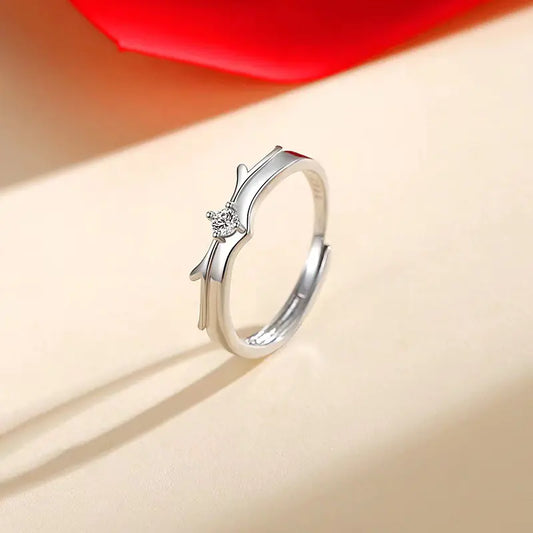 A silver ring with a small heart-shaped design on top, presented on a yellow background with a shadow.