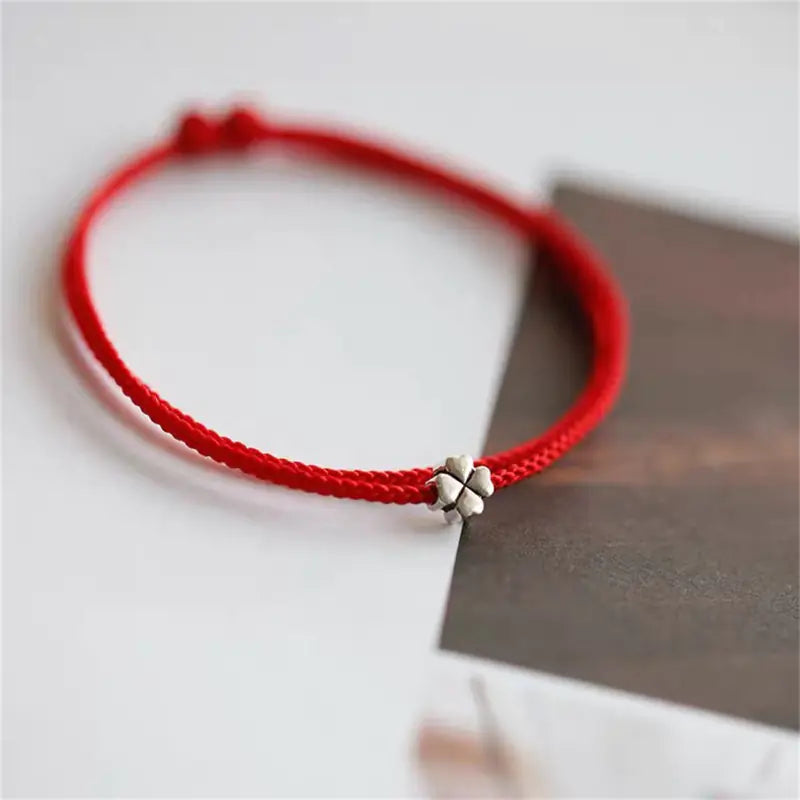 A simple woven hand rope bracelet with a floral shape and multicolored threads on a red background.
