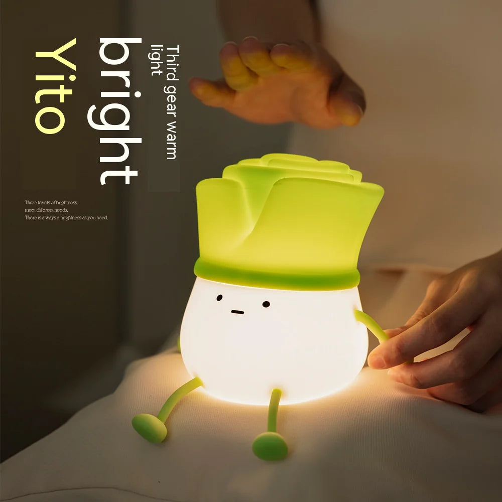 A green night light designed to resemble a stylized green onion, with a smiling face and cute arms, being held by a person.