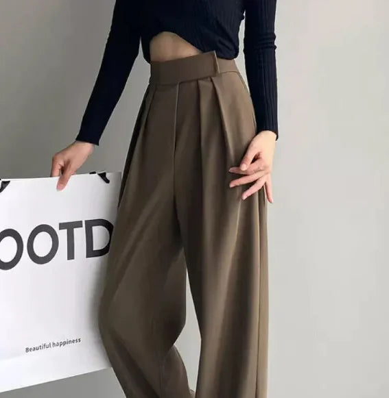 A person wearing high waist loose straight-leg pants in black color, paired with a crop top and white sneakers.