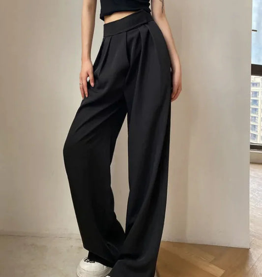 A person wearing high waist loose straight-leg pants in black color, paired with a crop top and white sneakers.