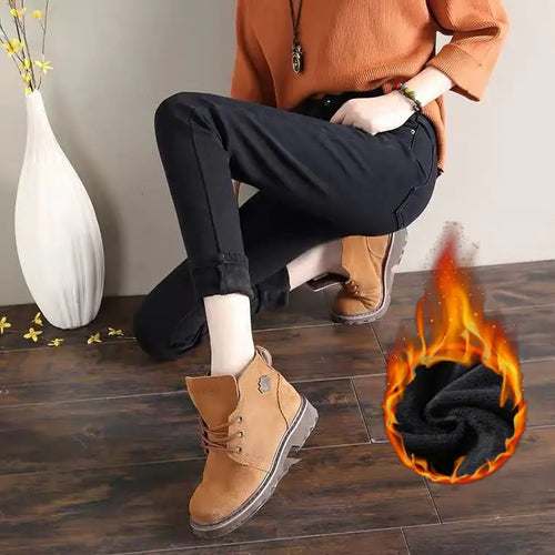 A pair of high-waisted plush jeans for women, in a dark color, styled with a pair of brown boots and an orange skirt, sitting against a wooden backdrop with a decorative item and a flame graphic effect on the image.