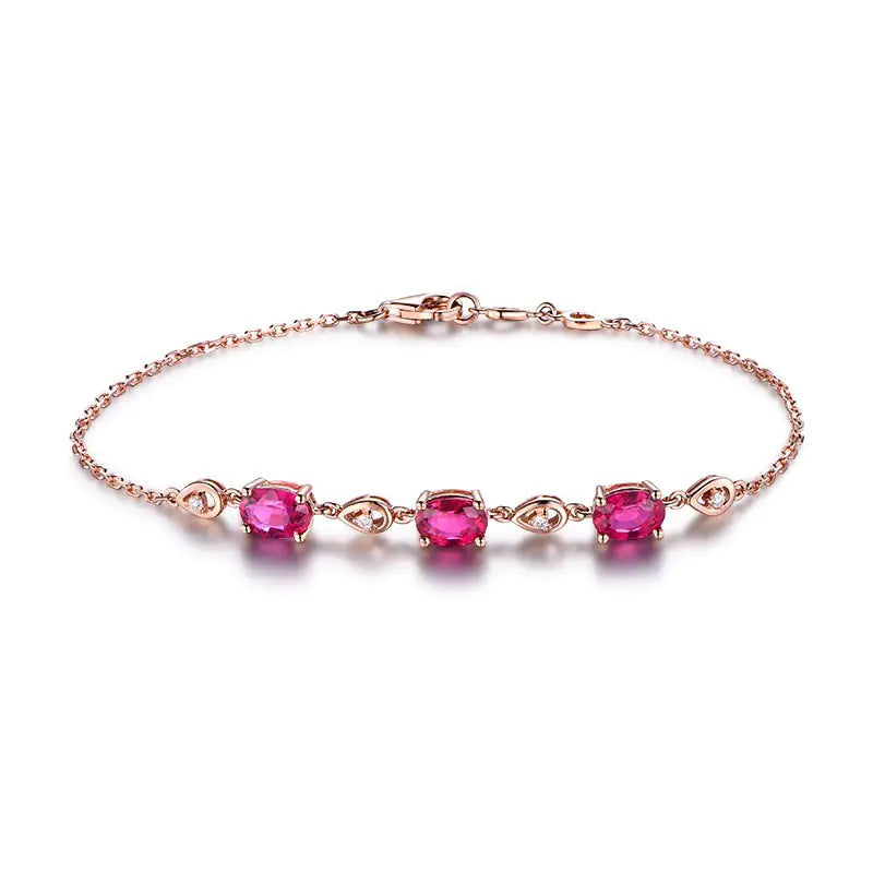 A hand wearing a rose gold-colored bracelet adorned with red tourmaline color gems.