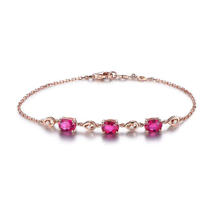 A hand wearing a rose gold-colored bracelet adorned with red tourmaline color gems.