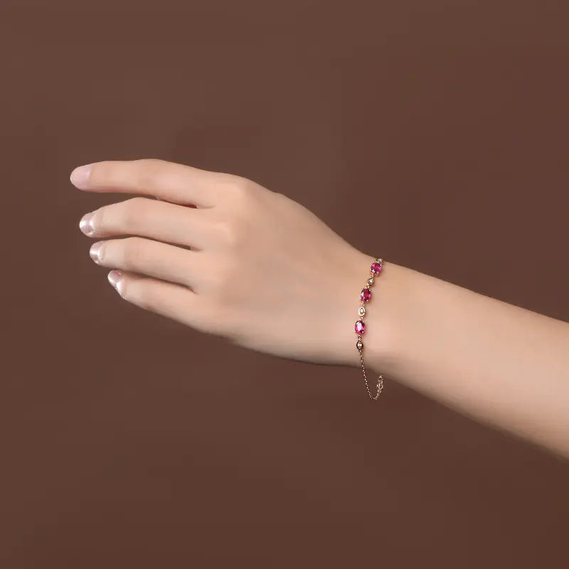 A hand wearing a rose gold-colored bracelet adorned with red tourmaline color gems.