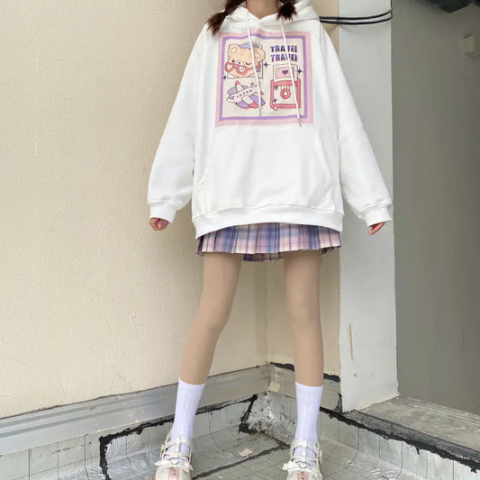 A woman wearing a white velvet sweater with a Japanese cartoon print, paired with a plaid skirt and white shoes.