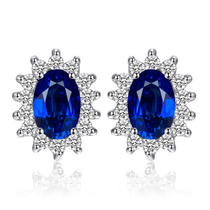 A pair of 14k gold plated 925 sterling silver stud earrings featuring blue sapphire gemstones surrounded by smaller clear crystals, designed in a princess diana or kate middleton style.
