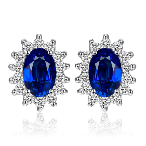 A pair of 14k gold plated 925 sterling silver stud earrings featuring blue sapphire gemstones surrounded by smaller clear crystals, designed in a princess diana or kate middleton style.