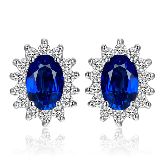 A pair of 14k gold plated 925 sterling silver stud earrings featuring blue sapphire gemstones surrounded by smaller clear crystals, designed in a princess diana or kate middleton style.