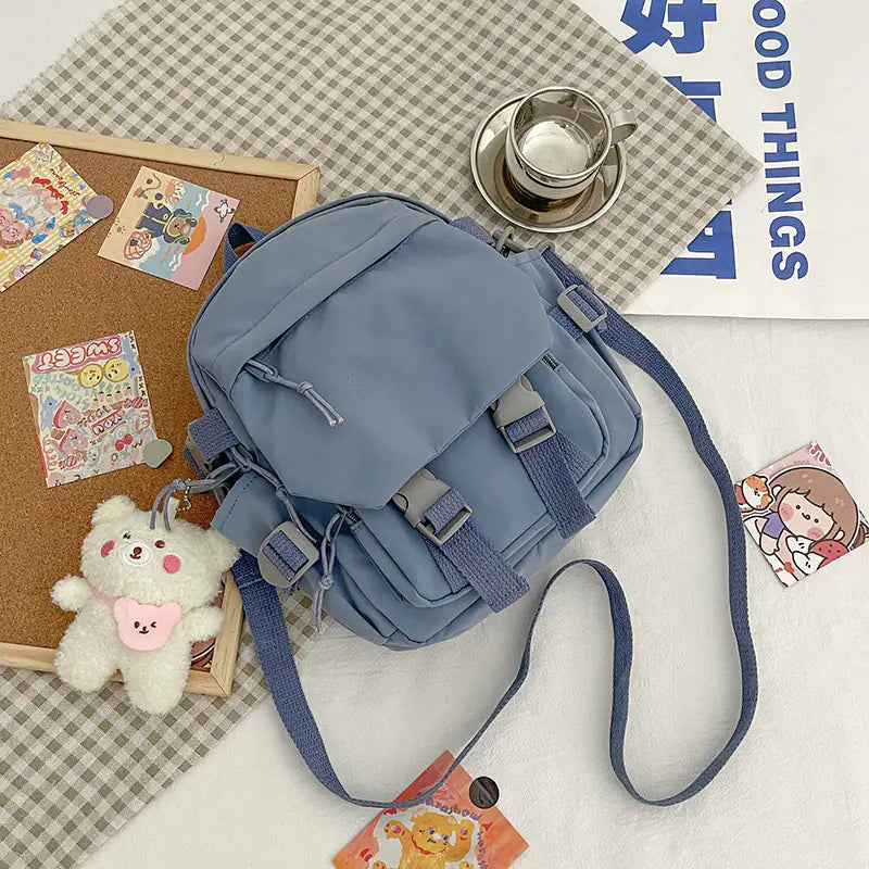 A pink Korean nylon oxford fabric literature backpack with a bear pendant, displayed alongside a camera, a notebook, and various accessories.