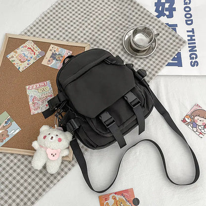 A pink Korean nylon oxford fabric literature backpack with a bear pendant, displayed alongside a camera, a notebook, and various accessories.