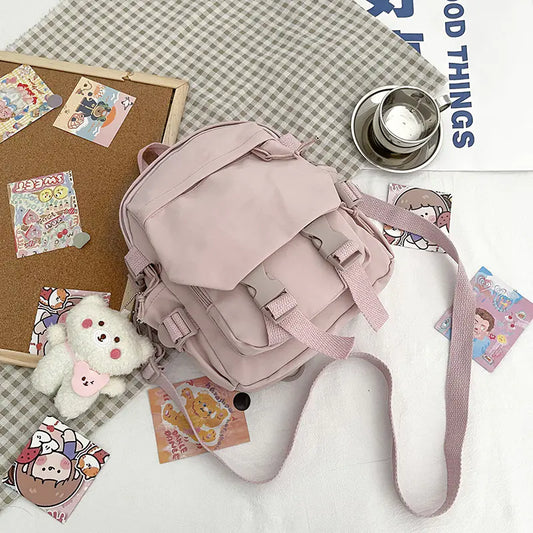 A pink Korean nylon oxford fabric literature backpack with a bear pendant, displayed alongside a camera, a notebook, and various accessories.