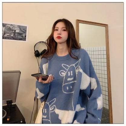 A woman wearing a blue loose pullover sweater with a cartoon pattern, holding a mobile phone.