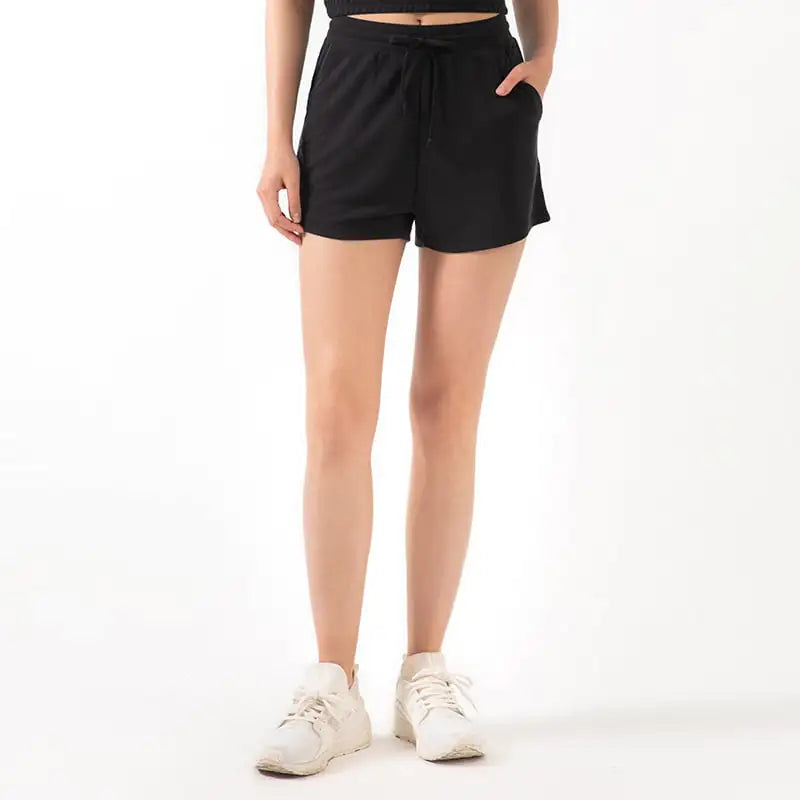 A pair of pink lace-wide loose yoga shorts with a drawstring waist, made from a modal fabric, paired with white sneakers.