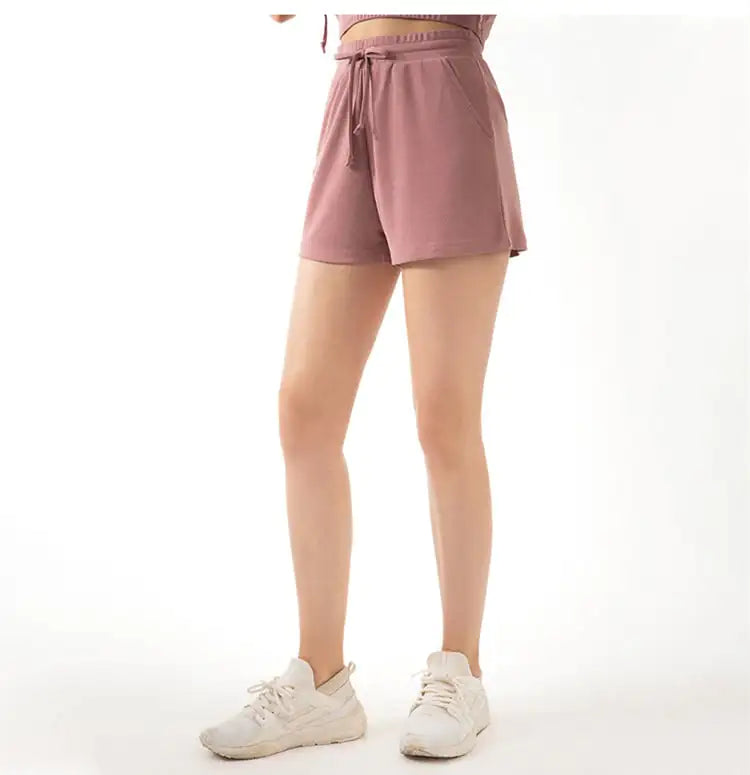 A pair of pink lace-wide loose yoga shorts with a drawstring waist, made from a modal fabric, paired with white sneakers.