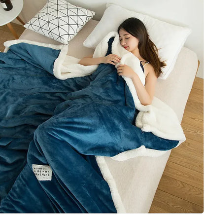 A person sitting on a bed with a pink flannel fleece blanket draped over them, displaying a plain pattern.