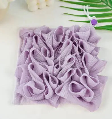 A purple loofah soap foaming net placed on a surface with a decorative element in the top right corner.