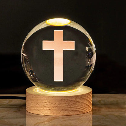 A luminous crystal globe with a cross design, glowing from within, placed on a wooden stand.