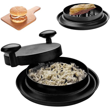 A person is using a black manual meat shredder to shred cooked chicken in a kitchen setting.