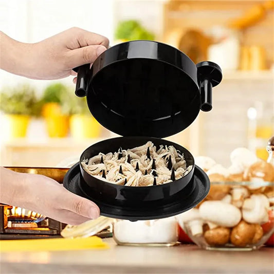 A person is using a black manual meat shredder to shred cooked chicken in a kitchen setting.