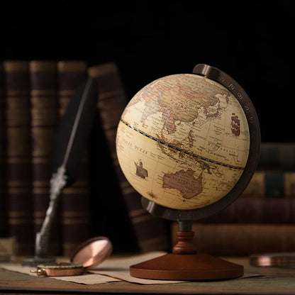A nostalgic English globe with traditional labeling, placed on a stand against a blurred background featuring old books and a pair of glasses.